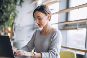 Mulher sentada em um café tomando café e trabalhando em um computador