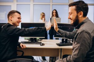 Ambiente corporativo com duas mulheres ao fundo e dois homens com um toque de mãos forma de colaboraçao